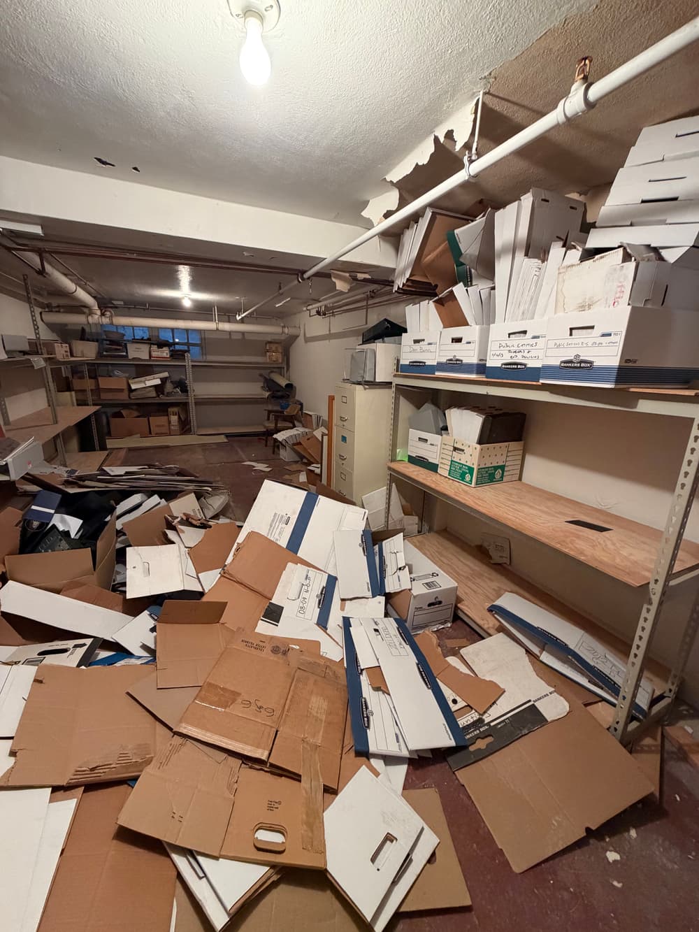 Cluttered storage room filled with piles of cardboard boxes and disorganized shelves.